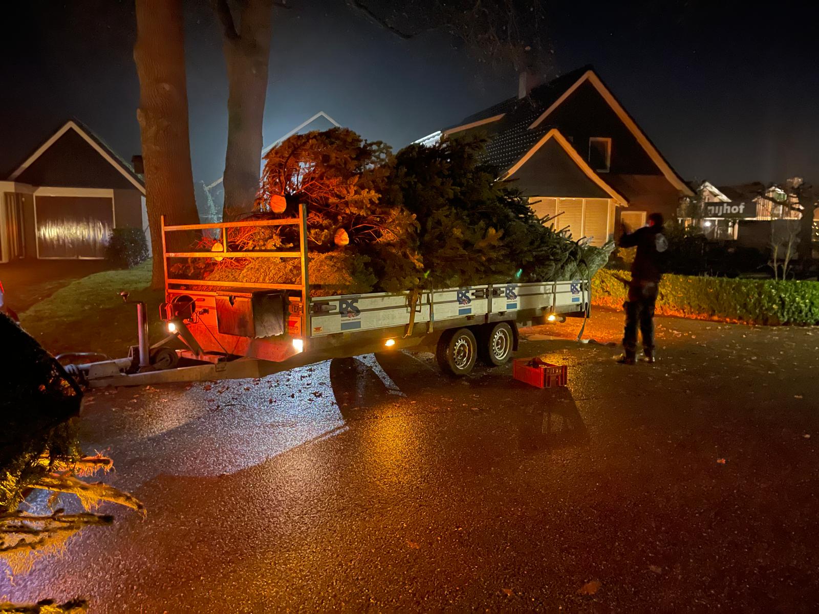 Volle aanhanger met kerstbomen tijdens een avondbezorging